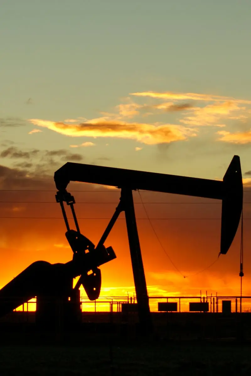 Dramatic silhouette of an oil pump jack against a vibrant sunset sky, emphasizing energy extraction.