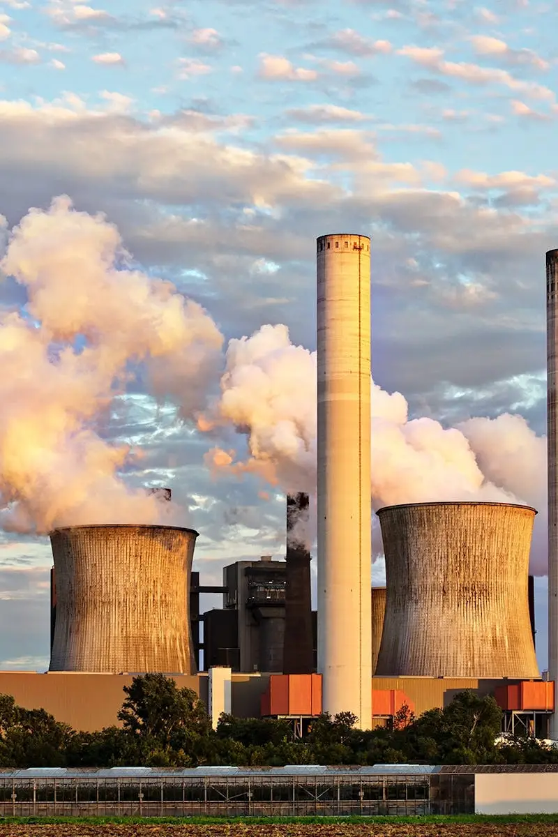 View of a power plant with smoke emissions under a cloudy sky, depicting industrial energy production.